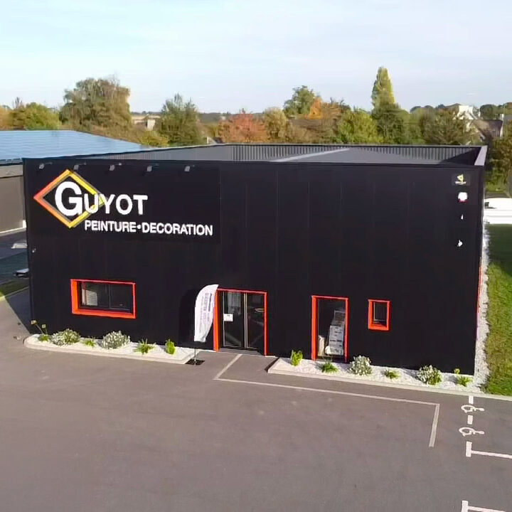 Vue aérienne des bureaux et du showroom Guyot Peinture Décoration à Pontivy, avec façade noire moderne, parking et espaces verts.